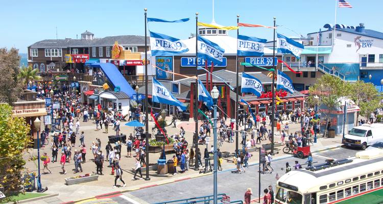 Des foules de visiteurs explorant le Pier 39 rempli de boutiques, de drapeaux et d'attractions colorées.