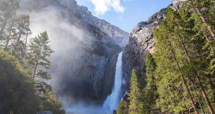 Puissante cascade se précipitant depuis des falaises de granit avec brume et sapins illuminés par le soleil.