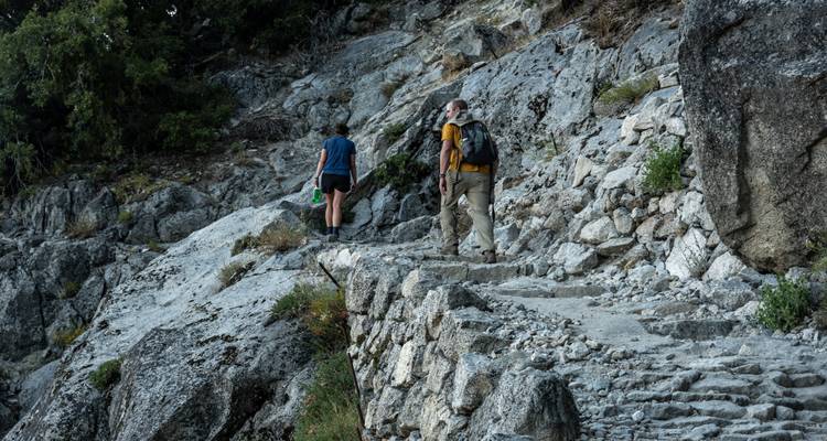 Des randonneurs montant un sentier de granit accidenté entouré de rochers et d'une végétation clairsemée.