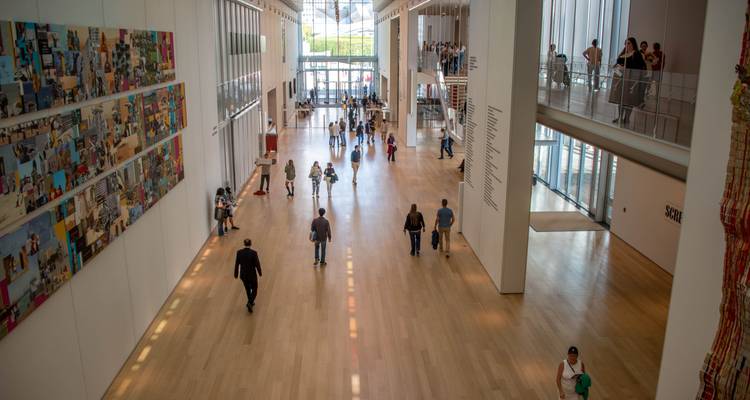 Vaste hall de musée d'art moderne avec des visiteurs marchant sur des planchers en bois poli.