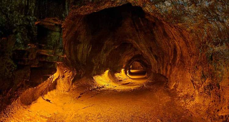 Long volcanic lava tube lit with warm orange lighting highlighting rough rock textures.