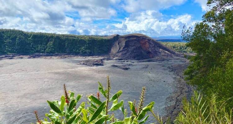 Wide view over a collapsed volcanic crater bordered by dense forest and bright clouds.