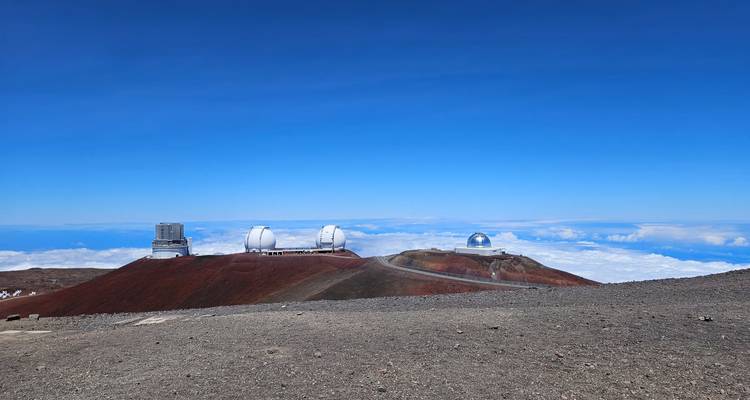 Observatory domes perched on a red volcanic ridge high above the clouds and ocean horizon.
