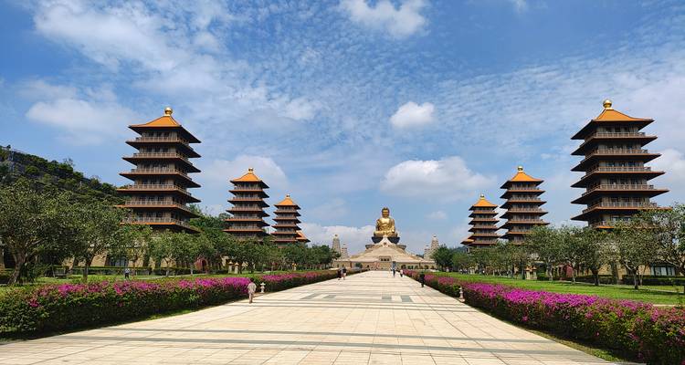 Gran bulevar bordeado de flores rosadas que lleva al enorme Buda sentado y las pagodas gemelas en Fo Guang Shan.