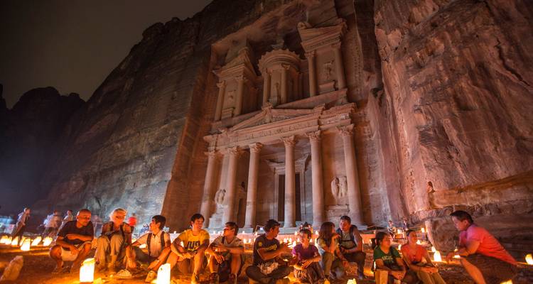 Besucher, die bei Kerzenlicht vor dem illuminierten Schatzhaus in Petra bei Nacht sitzen