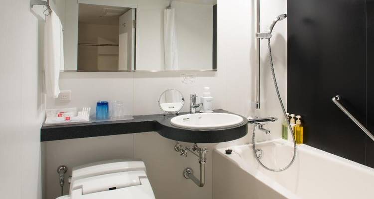 Modernes, kompaktes Hotelbadezimmer mit kombinierter Dusche und tiefem Badewanne, Waschbecken und hochmodernem WC.