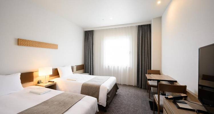Helles, minimalistisches Hotelzimmer mit zwei Einzelbetten, großem Fenster, neutraler Einrichtung und Arbeitsplatz.