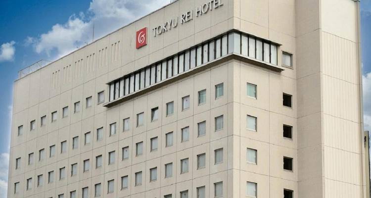 Außenansicht des mehrstöckigen Tokyu Rei Hotels vor blauem Himmel mit Markenbeschilderung.