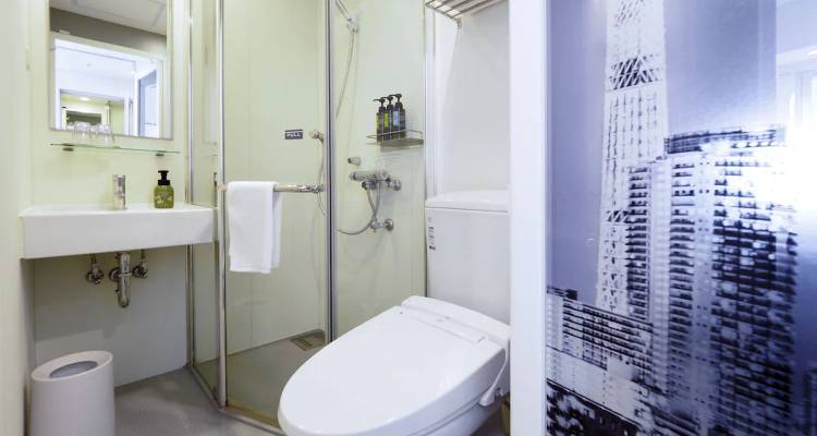 Kompaktes Badezimmer mit Glasdusche, Waschbecken und modernem WC mit bedrucktem Sichtschutzpaneel mit Stadtansicht.
