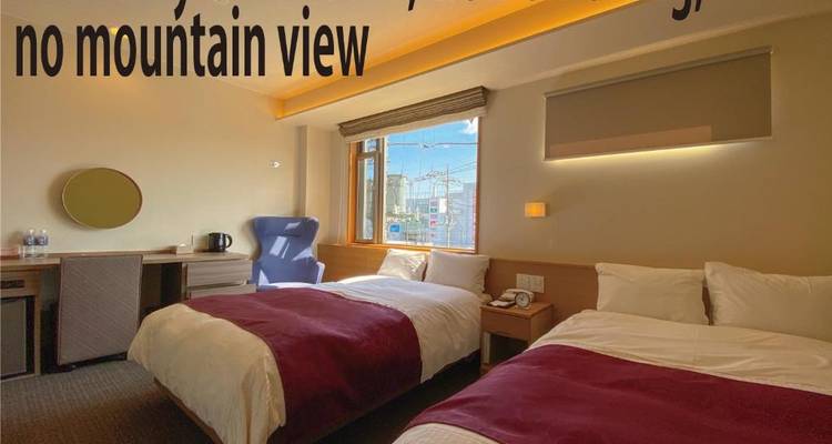 Hotelzimmer mit zwei Einzelbetten, fettgedrucktem überlagerten Text auf dem Bild und teilweisem Stadtblick durch das Fenster.