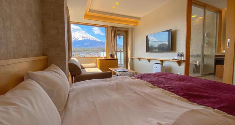 Gemütliches Hotelzimmer mit großem Fenster, das einen atemberaubenden Blick auf den Berg Fuji über der Stadt und dem See rahmt.