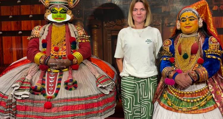 Tourist posiert mit zwei aufwändig kostümierten Kathakali-Performern in einer Theaterumgebung.