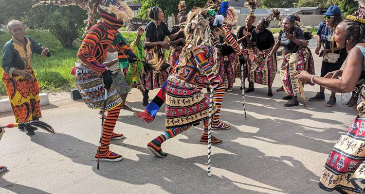Des danseurs aux costumes vibrants, vêtus de tenues rayées et perlées, exécutent une danse de rue énergique en Zambie.