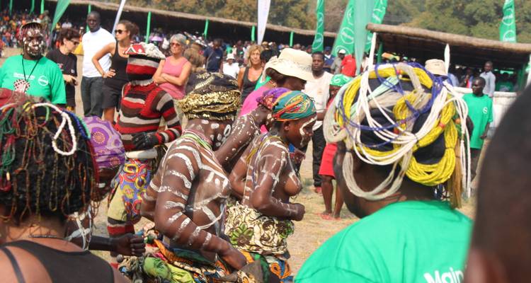 Grande foule lors d'un festival culturel avec des danseurs peints de motifs blancs et des spectateurs portant des chemises vertes.