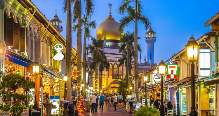 Lebhaft bewegte Abendszene im Kampong Glam in Singapur mit von Laternen beleuchteten Geschaeften und der goldenen Kuppel der Sultan-Moschee, die sich majestaetisch davor erhebt.