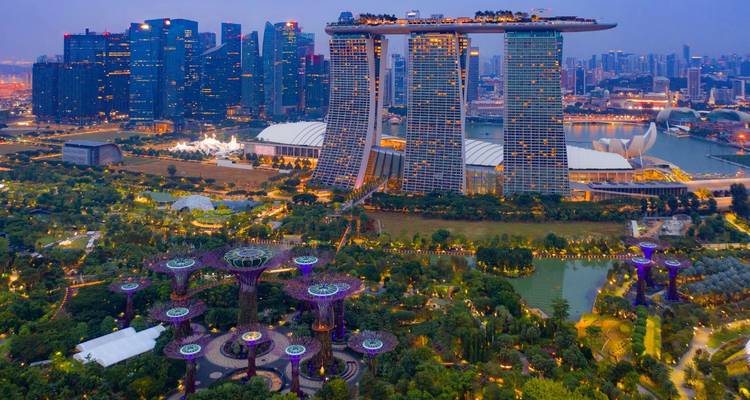 Luftaufnahme bei Einbruch der Dunkelheit des Marina Bay Sands, das sich über dem beleuchteten Supertree Grove und der Skyline der Stadt erhebt.