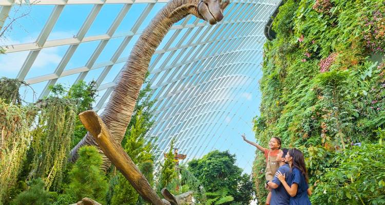 Ein Erwachsener und ein Kind bewundern ein imposantes Sauropoden-Modell inmitten üppiger Vegetation unter einem gewölbten Glasdach.