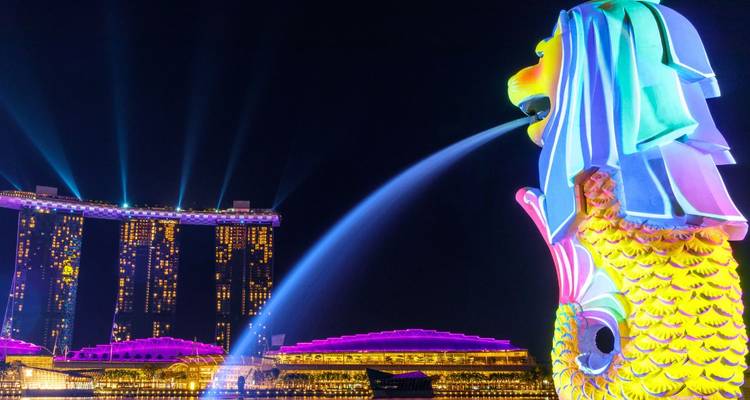 Die farbenfrohe Merlion-Statue spritzt Wasser in Richtung der beleuchteten Marina Bay Sands Türme während einer beeindruckenden Lichtshow in der Nacht.