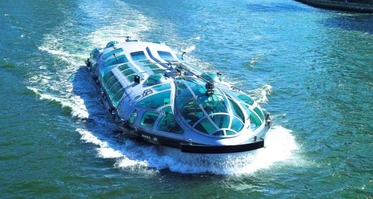 Ein futuristischer Wasserbus mit Glaskuppel flitzt über Tokyos Sumida-Fluss und erzeugt dabei schäumende Wellen.
