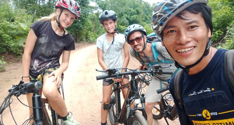 Selfie de groupe souriant de quatre cyclistes tenant des vélos de montagne sur un chemin de terre entouré de verdure
