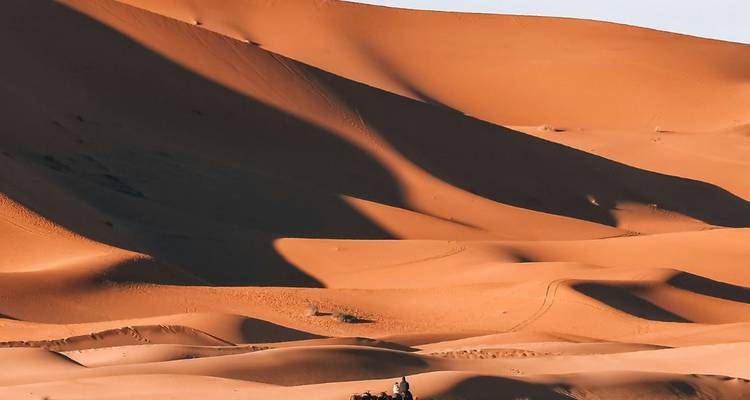 Uitgestrekte zandduinen met dramatisch licht en een eenzame kamelenier die klein lijkt in het immense woestijnlandschap