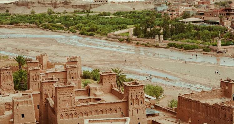 Panoramisch uitzicht op het oude versterkte dorp Aït Benhaddou naast een droge riverbedding en weelderige palmen