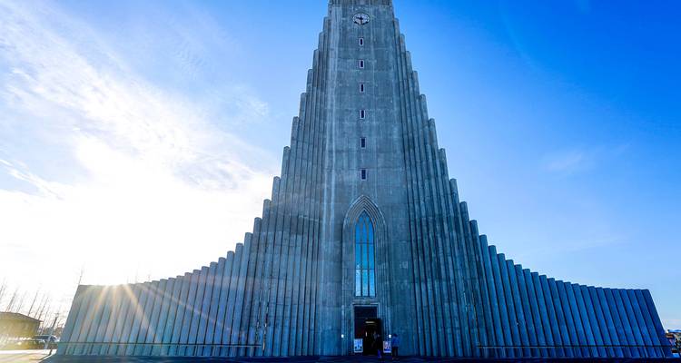 Frontansicht der Hallgrimskirkja-Kirche, die in einen hellen Himmel emporsteigt, mit Sonnenstrahlen, die an ihrer Basis aufblitzen