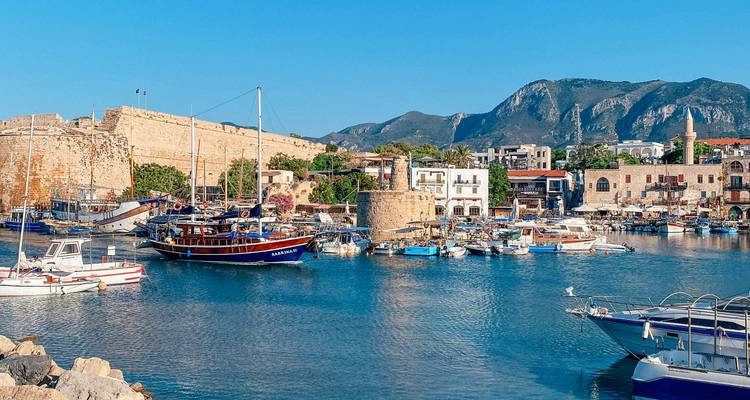 Puerto de Kyrenia con yates amarrados, muros del fuerte medieval y un telón de fondo de montañas escarpadas en una tarde soleada