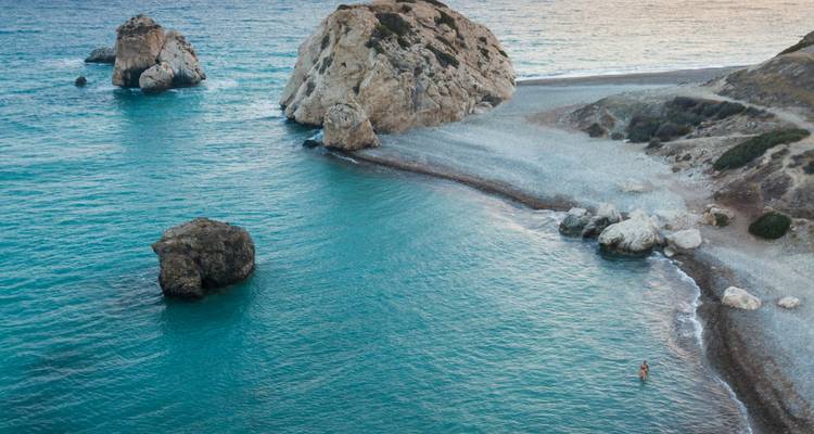 Escena tranquila de la Roca de Afrodita con olas suaves y un nadador solitario en aguas azul cristalino