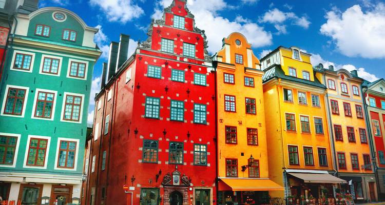 Reihe von hell angestrichenen historischen Stadthäusern vor einem lebendigen blauen Himmel in Stockholms Altstadt