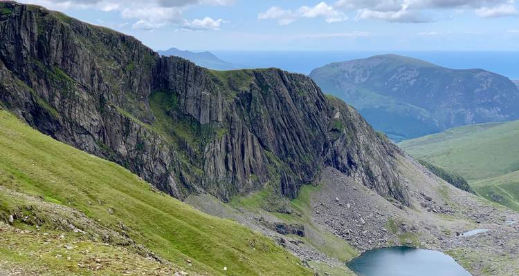 Los acantilados verdes y empinados caen hacia un lago glacial en las montañas escarpadas de Snowdonia.