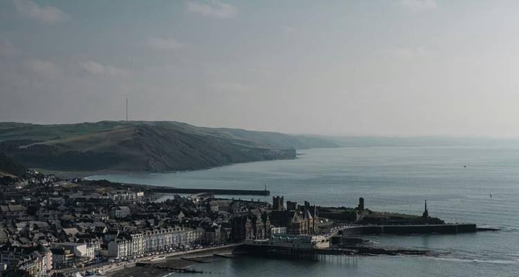 Panorama costera brumosa de Aberystwyth con paseo marítimo y promontorios ondulantes que se extienden hacia la distancia.