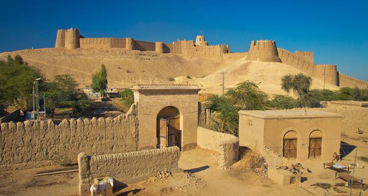 Les imposantes murailles de la forteresse désertique s'étendent sur une colline aride sous un ciel bleu éclatant.