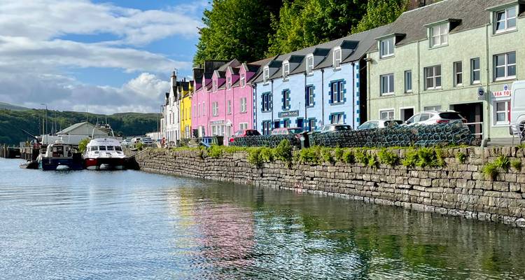Rangée de maisons pastel du front de mer se reflétant dans l'eau calme du port de Portree.
