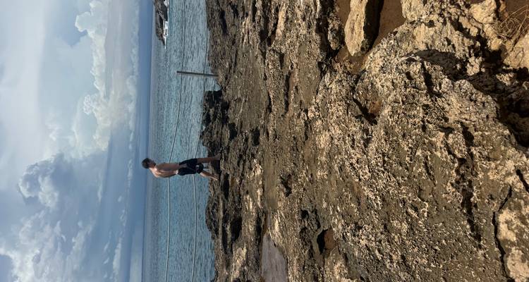 Un hombre caminando sobre rocas volcánicas accidentadas cerca de una barrera de cuerda con el océano de fondo.