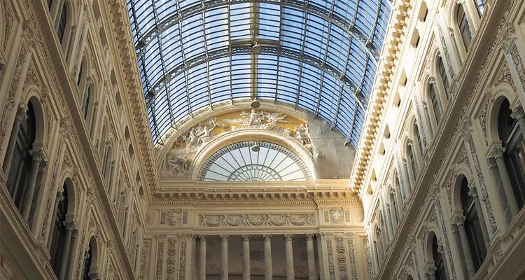 Elegantes Interieur einer großen Arkade mit verzierter Fassade und einer geschwungenen Glaskuppel, die Sonnenlicht hereinlässt.