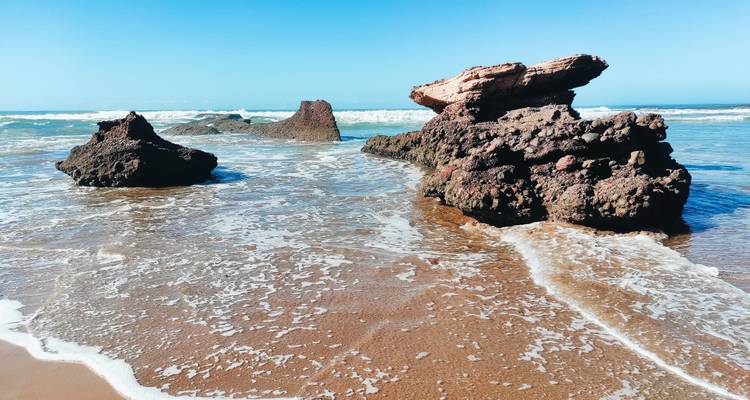 Les vagues se brisent sur les formations rocheuses dentelées qui émergent d'un rivage sablonneux.