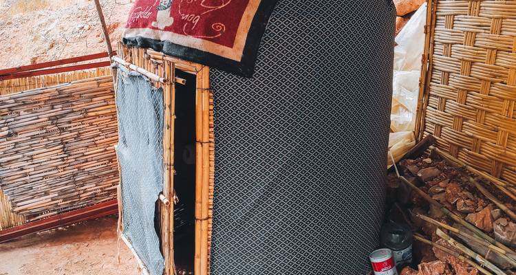 Petite hutte de vapeur improvisée construite à partir de bambou, de tissu et de tapis à côté de fournitures empilées.