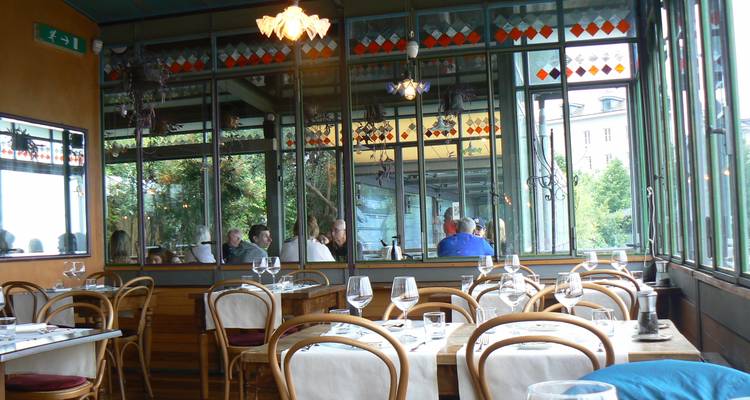 Elegantes Restaurantinneres mit Glasswaenden, eingedeckten Tischen und Gaesten, die sich in grossen Spiegeln widerspiegeln.