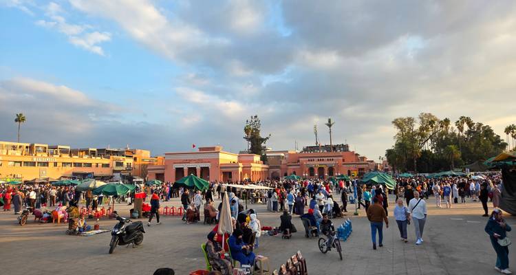 Drukke Jemaa el-Fnaa-plein vol met mensen, voedselkraampjes en artiesten onder een dramatische lucht.