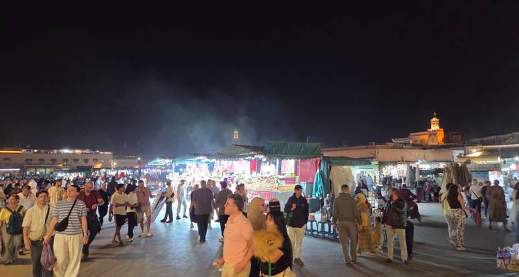 Drukke nachtscène op het Jemaa el-Fna plein met eetkraampjes, rook en menigte onder de donkere hemel.