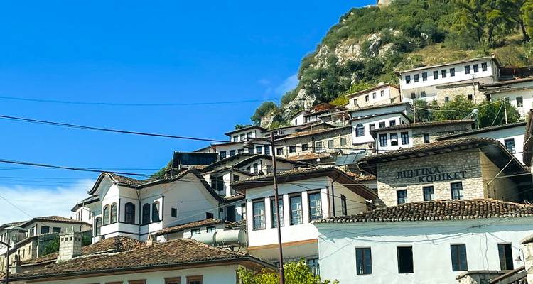 Casas blancas de estilo otomano tradicional subiendo por una ladera verde bajo un cielo azul.