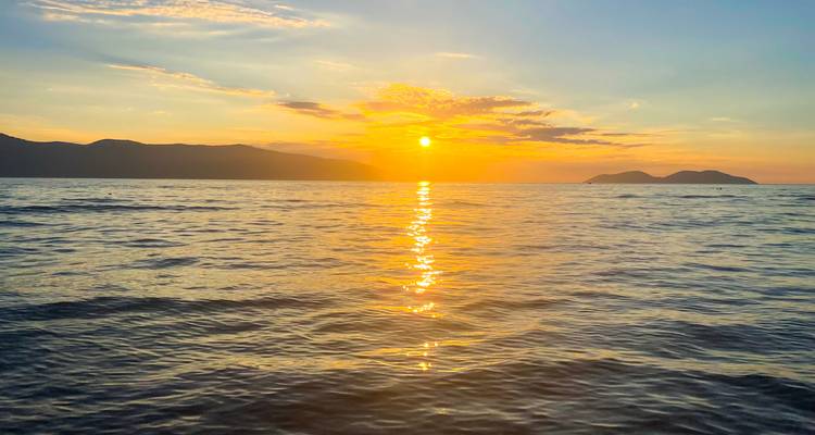 Soleil orange ardent se couchant sur une mer calme créant des reflets dorés.