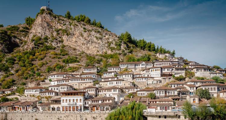 La ville historique perchée de Berat avec ses rangées de maisons blanches ottomanes situées sous une falaise rocheuse et des pins.