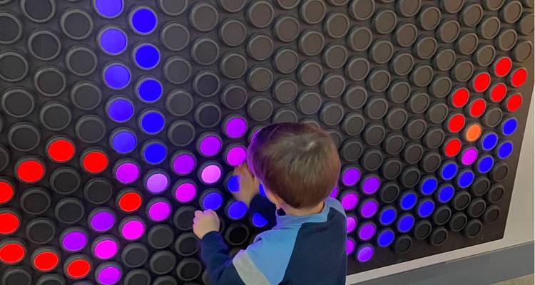 L'enfant place des chevilles colorées dans un grand panneau illuminé dans une exposition interactive de musée.