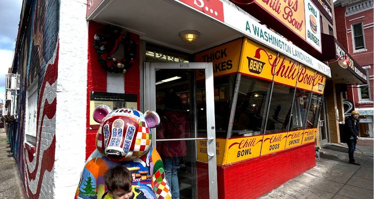Façade colorée de Ben's Chili Bowl avec une statue d'ours peinte et un enfant debout à l'entrée.