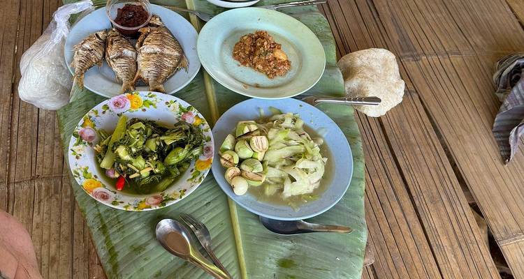 Repas traditionnel laotien disposé sur une table en bambou recouverte de feuilles de bananier, comprenant du poisson grillé, des légumes et des sauces.