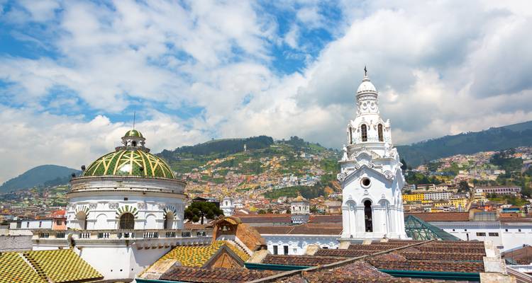 Dômes et clocher blanc de églises historiques à Quito avec des collines vertes en arrière-plan.