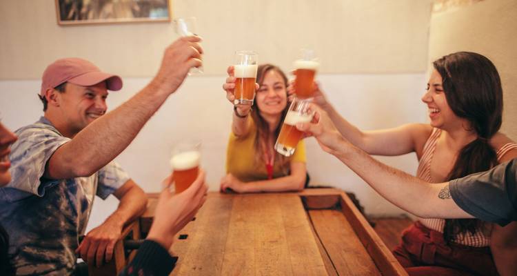 Amigos sentados alrededor de una mesa de madera brindando con vasos de cerveza en un acogedor ambiente de bar.
