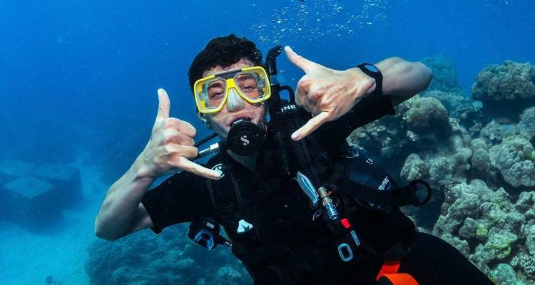 Plongeur en scaphandre autonome signalant sous l'eau au milieu de formations de corail vibrant et d'eau bleu clair.